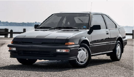 1986-1989 Acura Integra 2dr H/B in black parked near water, showcasing sleek design and classic styling.